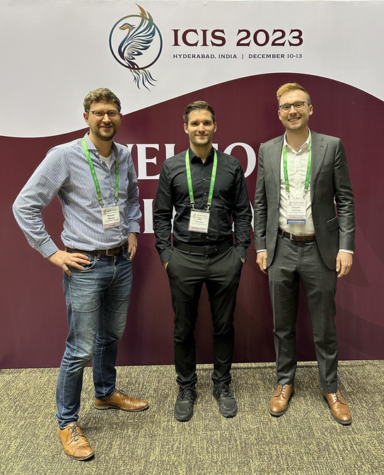 ICIS 2023 Manuel Wiesche, Kay Hönemann und Vincent Heimburg vor dem ICIS 2023 Logo