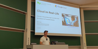 Dr. Marcus Roy hinter einem Pult, im Hintergrund die erste Slide mit dem Titel seiner Präsentation