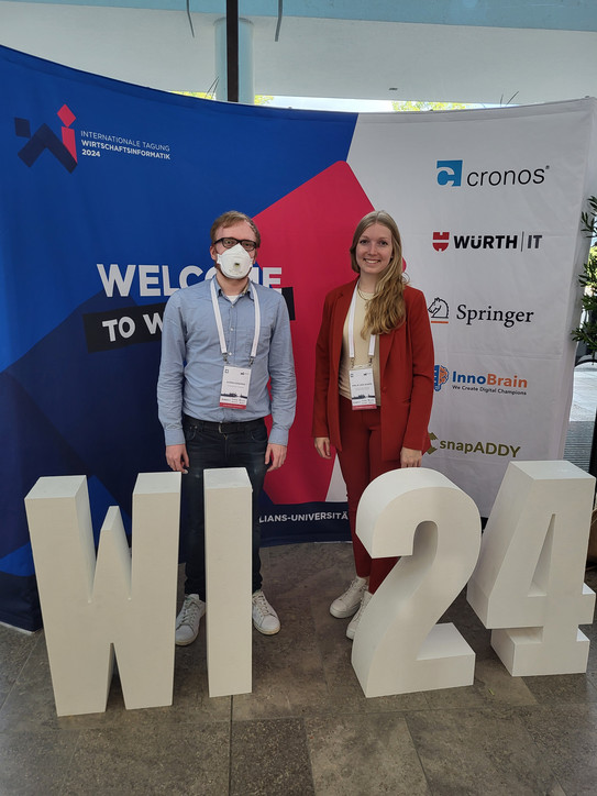 Björn Konopka und Amelie Schmidt vor WI 24 Konferenz Logo