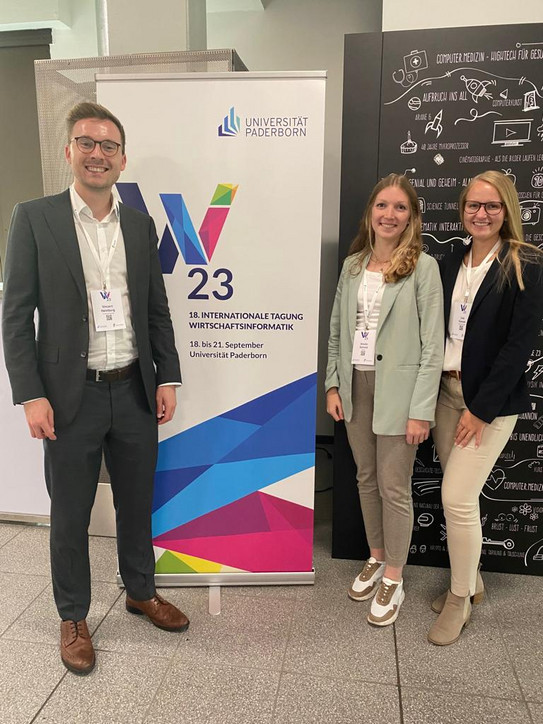 Vincent Heimburg, Amelie Schmid and Lisa Gussek in front of a banner of WI 2023