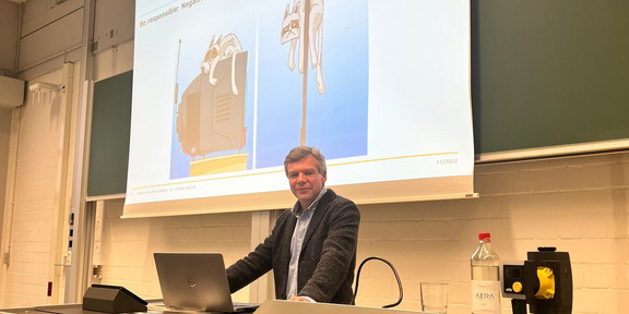 Dr. Thorsten Kettner at the lectern in front of the screen in the lecture hall, on which two pictures are displayed for the heading "Be responsible: negative impact of innovations