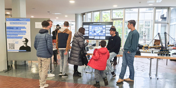 Open Day 2024 - Picture of people in front of participation table, with project posters in the background.