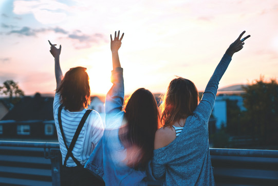 Photo of three young people from behind, arms in the air, friends