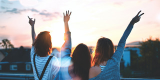 Photo of three young people from behind, arms in the air, friends