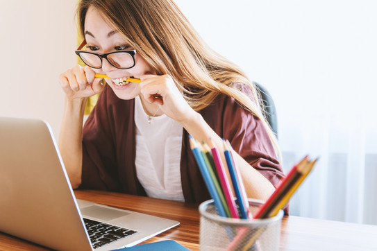 Photo: Woman looking at her laptop screen, nervously chewing on a pencil