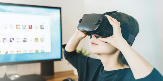 Frau mit VR Brille, im Hintergrund Monitor mit Desktop auf Bildschirm