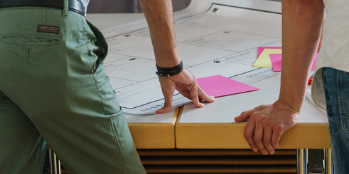 Photo of two people leaning with their hands on a table with plans