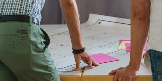 Photo of two people leaning with their hands on a table with plans