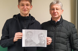 Two men in front of a wall. They are holding a picture of themselves made up of dominoes.