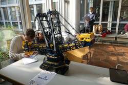 Junger Mann macht Notizen hinter einem Lego Kran. Vor ihm liegt ein Hinweis zum WizARd Projekt.