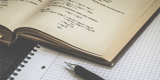 Aufgeschlagenes Mathematikbuch mit schwarzem Stift und karriertem Papier. 