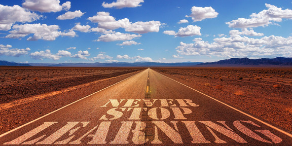 Foto einer schnrugreraden Straße bis zum Horizont in einer steppenartigen Einöde, auf die der Text "Never Stop Learning" geschrieben wurde