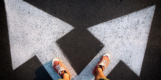 Someone stands with his feet at the beginning of two arrows pointing in different directions
