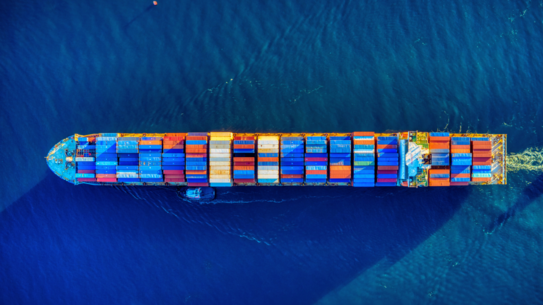 Photo: Container ship with colorful containers, photographed from above, on blue water.
