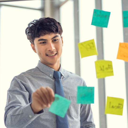 Junger Mann vor Post-Its auf Glaswand geklebt. 