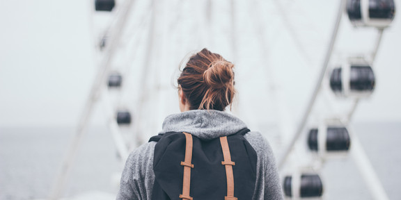 Frau mit Rucksack, von hinten fotografiert, vor Riesenrad