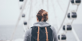 Frau mit Rucksack, von hinten fotografiert, vor Riesenrad