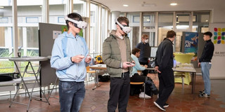 Two people wearing VR headsets in the Audimax foyer.