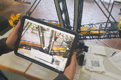 Person hält Tablet mit Bild von Bagger vor Modellbagger