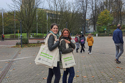 Two women on the TU Dortmund campus. They are carrying cloth bags with the words “Work where others study” printed on them.