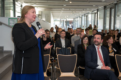 Prof. Liudvika Leišytė mit Mikrofon in der Hand stellt Fragen. Im Hintergrund ist das Publikum zu sehen.