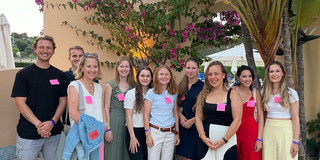 Group of students and doctoral candidates in front of a wall with a gate and plants.