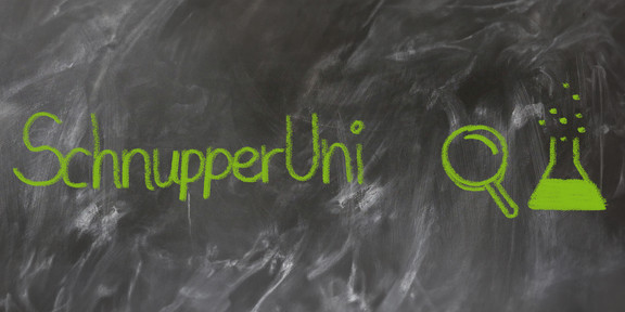The text "SchnupperUni" written in green chalk on a not quite cleanly wiped blackboard, next to it a painted magnifying glass and a half-filled test tube