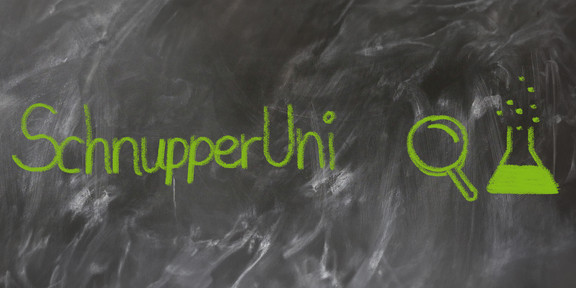 Mit grüner Kreide auf nicht ganz sauber gewischter Tafel geschriebener Text "SchnupperUni" , daneben eine gemalte Lupe und ein halb gefülltes Reagenzglas