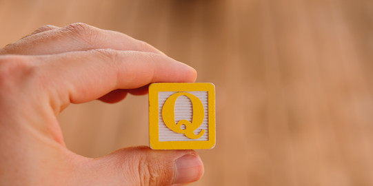 Photo: Hand holding a square with the letter Q in the middle.