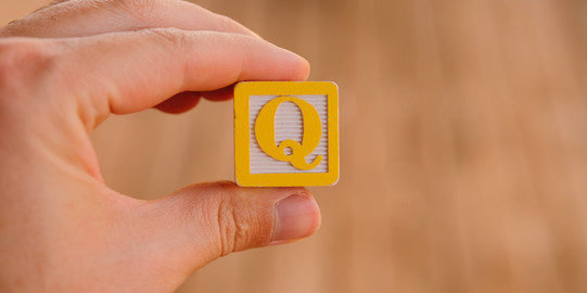 Photo: Hand holding a square with the letter Q in the middle.