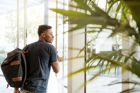 Photo: Young man with backpack walks through glass door, palm tree in side foreground