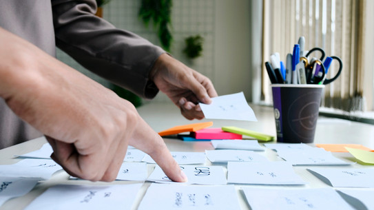 Photo: Two people's hands point to Post-its stuck on a table in front of them.