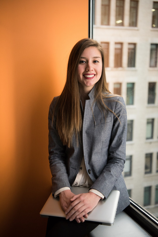 Photo: Woman in business attire, sitting at a window, laptop on her lap.