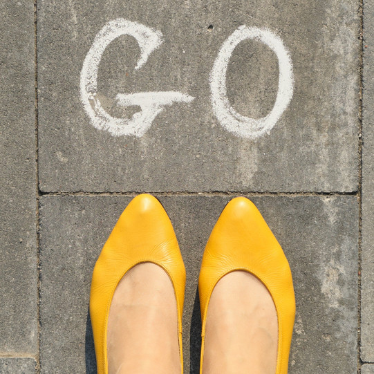 Photo: Women's feet in yellow ballerinas, on cobblestones, with the word "Go" written in chalk in front of them.