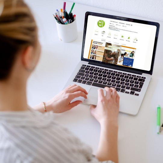 Am Schreibtisch sitzende Studentin tippt auf dem Laptop, daneben liegen Bücher und Stifte. Auf dem Bildschirm ist der WiWi Instagram Account zu sehen.