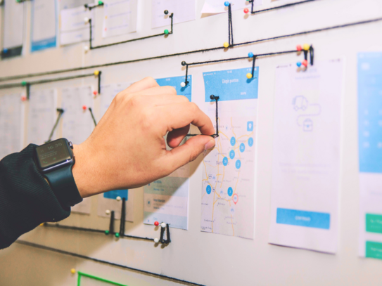 Photo: Hand connects printouts with information using threads and pins.