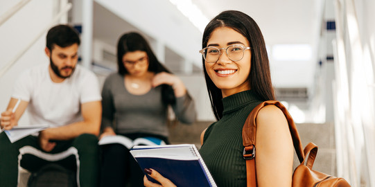 Young smiling woman with notes, two other people in the background.