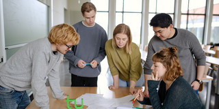 Five students stand around a table and look at a piece of paper.