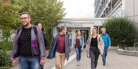 Six students are walking out of the auditorium building.