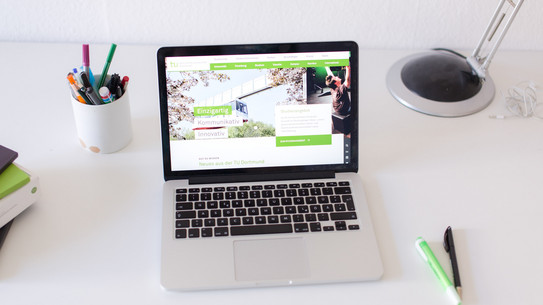 Arbeitsplatz am Schreibtisch, mit eingeschaltetem Laptop und Stiften.