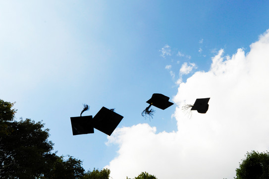 Four black doctor hats flying in the air in front of blue sky with white clouds.