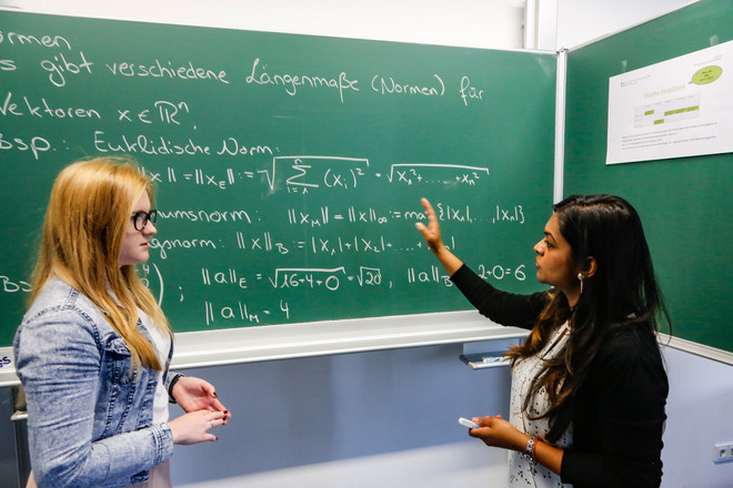 Two students are standing in front of a blackboard.