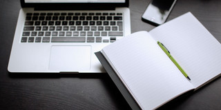 Laptop, Smartphone und Notizbuch mit Stift auf einem Tisch liegend.