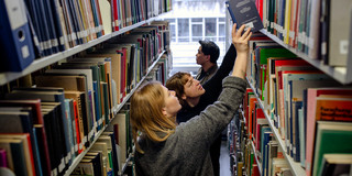 Studierende suchen nach Büchern in Bücherregalen in der Bibliothek.