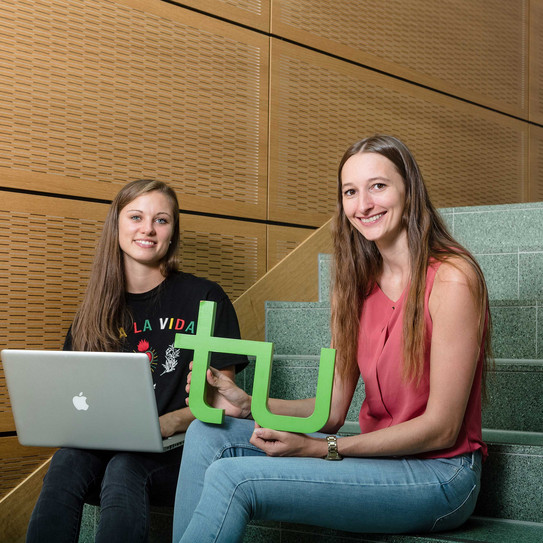 Studentinnen mit Laptop und TU-Logo Zwei Studentinnen sitzen mit Laptop und TU-Logo auf einer Treppe.