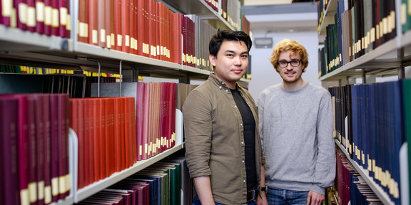 Zwei Studierende in der Bibliothek Zwei Studierende stehen zwischen zwei Bücherregalen in der Bibliothek.