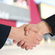 Two shaking hands. A building and a blue sky can be seen in the background.