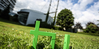 TU-Logo Im Vordergrund steht das TU-Logo im Gras, im Hintergrund das Audimax.