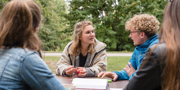 Vier Studierende sitzen draußen an einem Tisch und lernen zusammen.