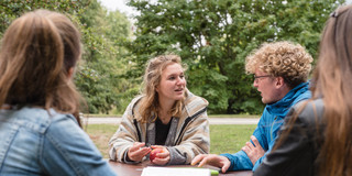 Vier Studierende sitzen draußen an einem Tisch und lernen zusammen.